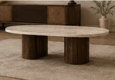 Travertine Oval Coffee Table with a natural stone top and two ribbed dark wood cylindrical supports in a contemporary living room.