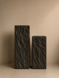 Set of two black textured display pedestals with antique gold detailing, featuring a rugged rock-inspired finish in two different heights.
