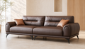 Espresso brown three-seater leatherette lounge sofa with rounded arms, soft segmented back cushions, caramel throw cushions and slim black metal legs.