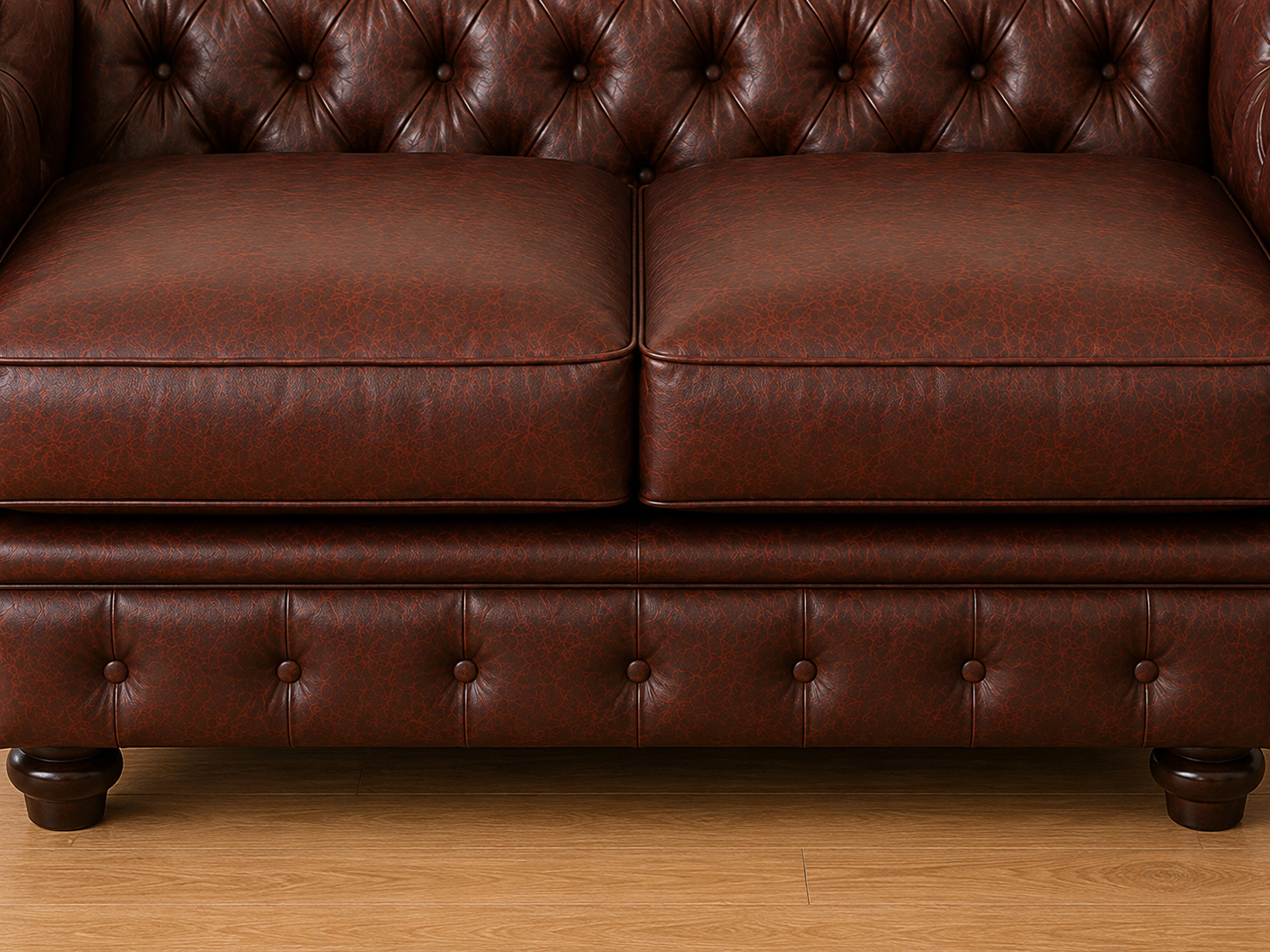 A close-up of a dark brown leather Chesterfield sofa, showing the tufted backrest, two seat cushions, and the matching tufted base with dark wooden legs on a light wood floor.