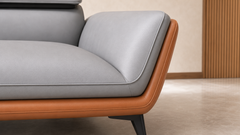 Close-up of a modern sofa corner showing light gray leather cushions and a warm tan leather frame, with a dark metal leg in a minimalist indoor setting.