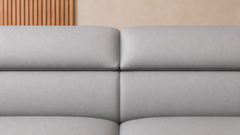 Close-up of a light gray upholstered sofa with padded back cushions and a neutral indoor background.