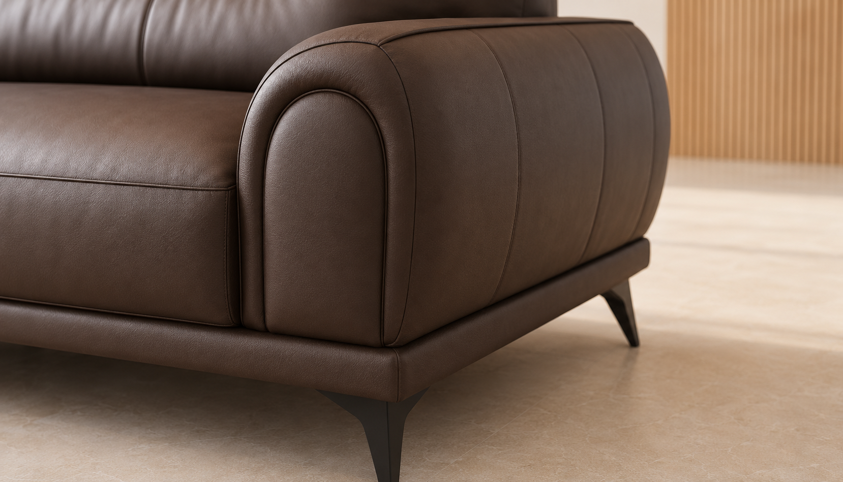 Close-up of a dark brown leather sofa showing the rounded armrest, stitched paneling, and dark metal legs on a light beige floor.