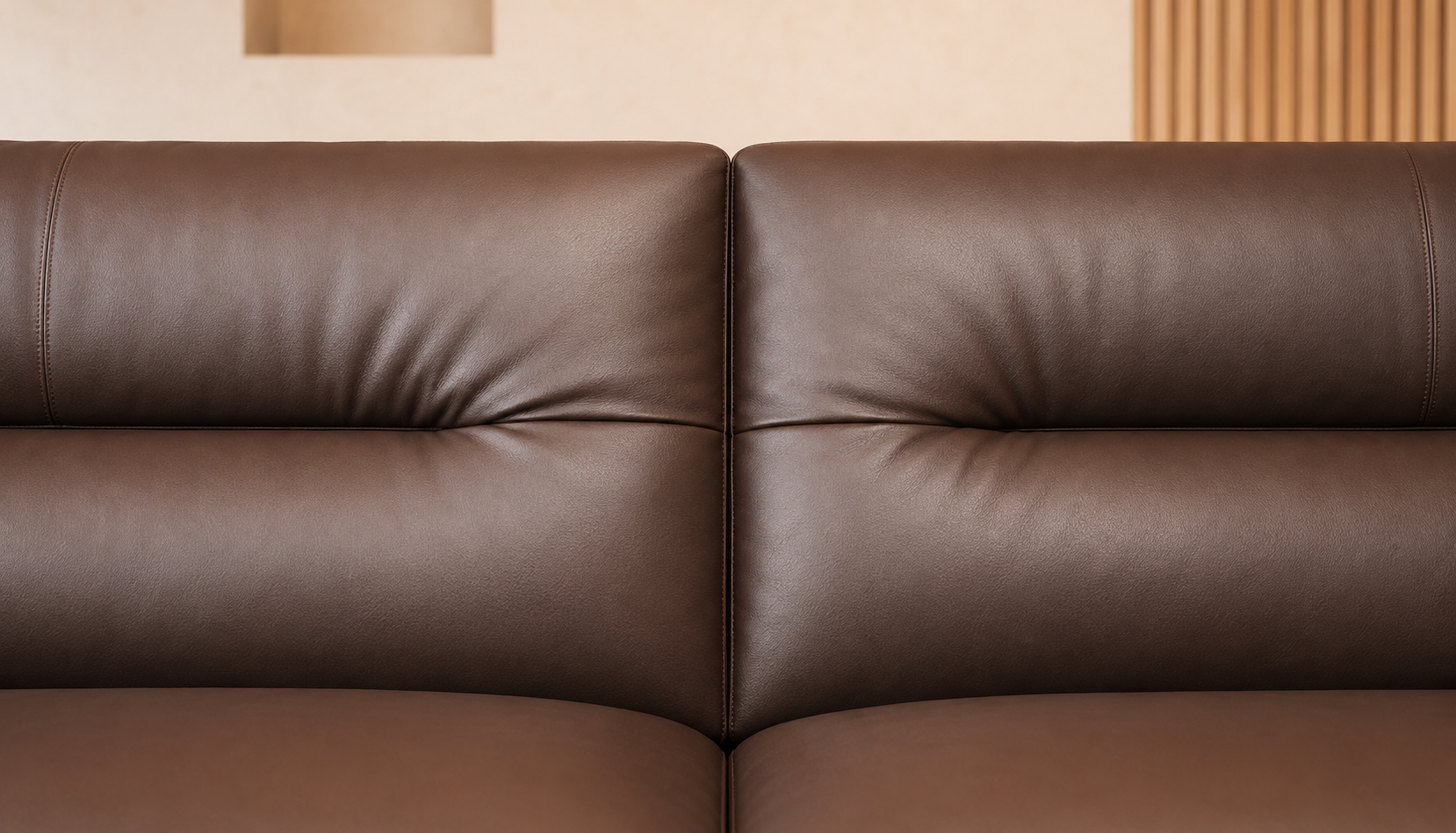 Close-up of a brown leather sofa showing the tufted back cushions and smooth seat surface in a warm indoor setting.