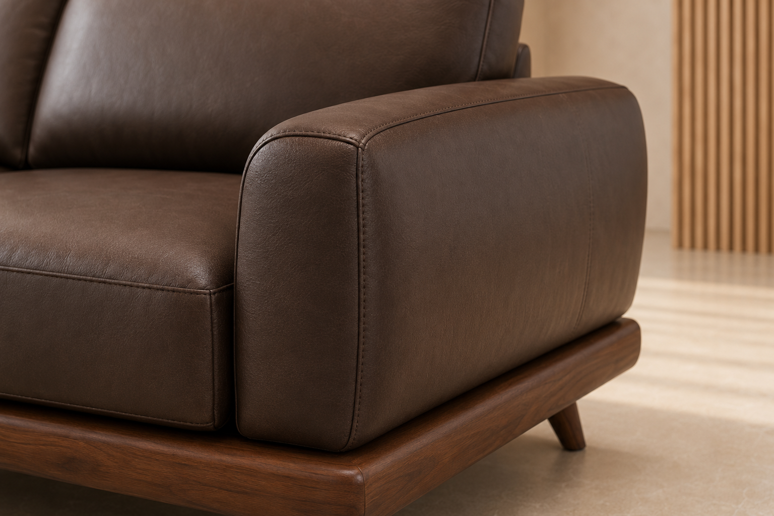 Close-up of a dark brown leather sofa armrest with a wooden base and leg, shown in a modern interior setting.