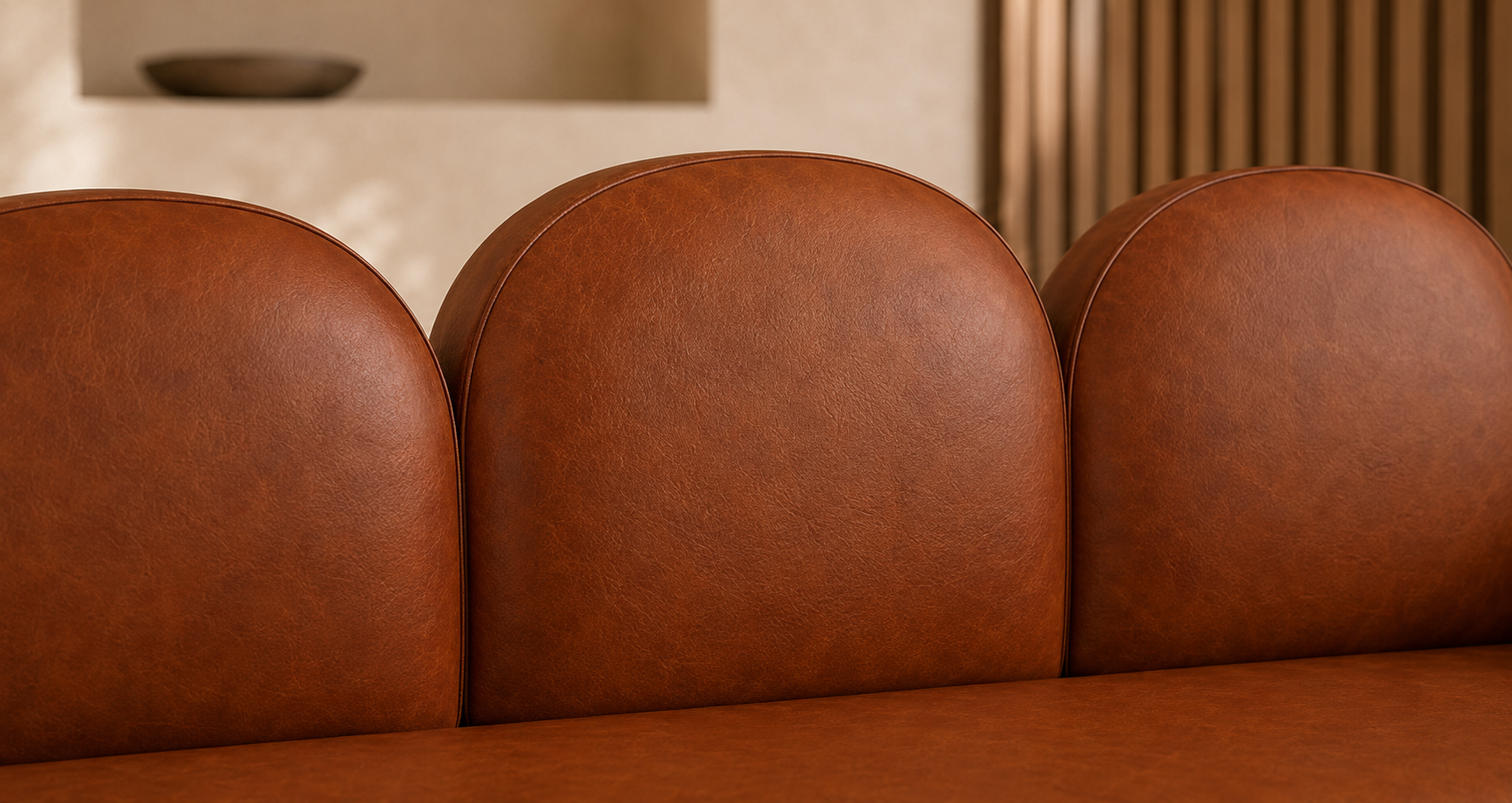 Close-up of a brown leather sofa with three rounded back cushions and a matching seat cushion in a warm interior setting.