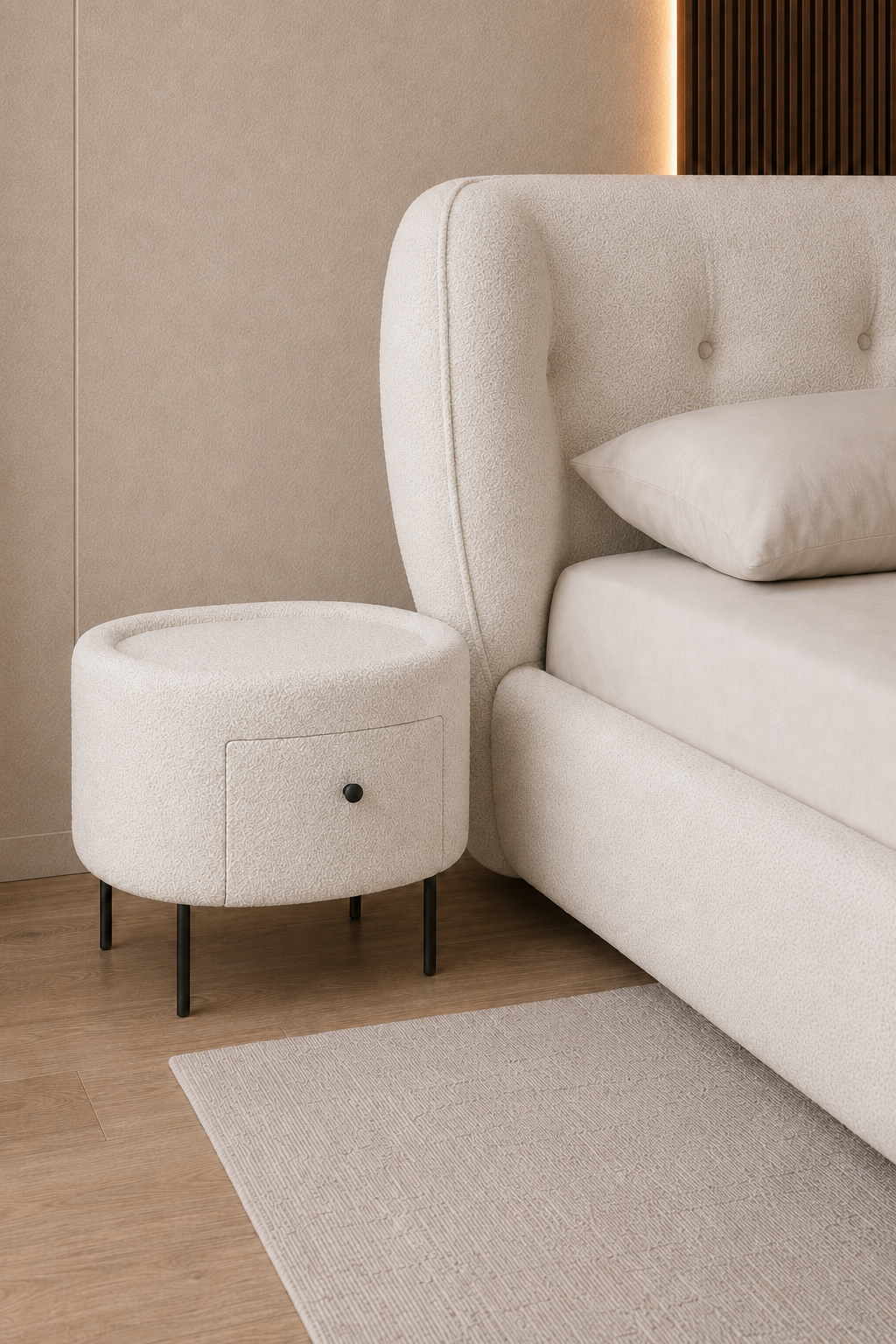 A modern bedroom scene featuring a round upholstered ottoman nightstand with black metal legs next to a tufted bed headboard in a minimalist beige room.