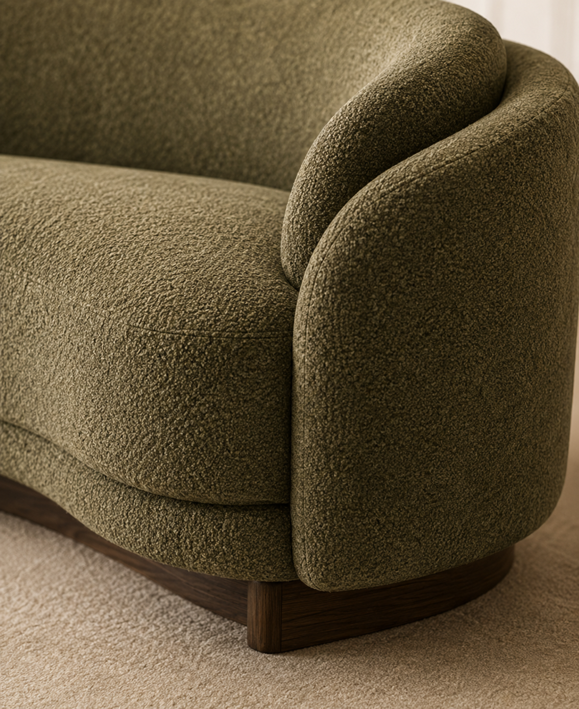 Close-up of a curved upholstered sofa arm in textured olive green fabric, showing the fabric texture and a dark wood base on a beige carpet.